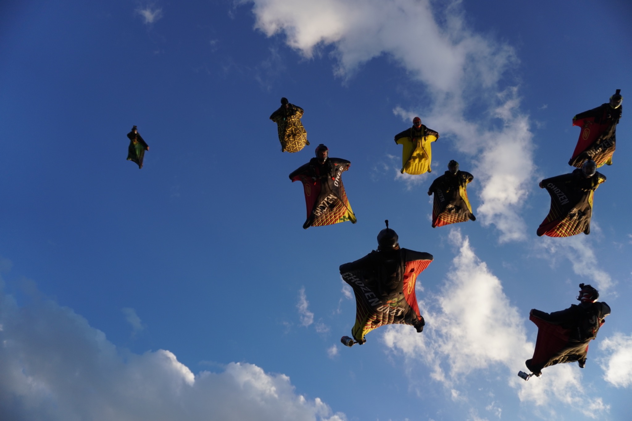 Chozen Ones wingsuit flyers together in a big flock against the evening sky